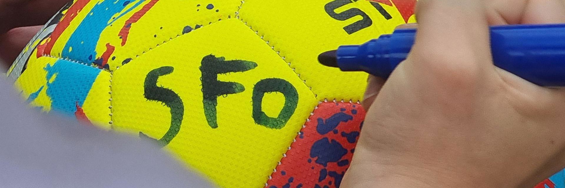 Billede af et barns hænder, der skriver SFO på en fodbold